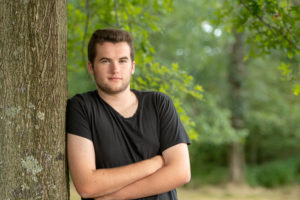 senior boy leaning a tree black t-shirt